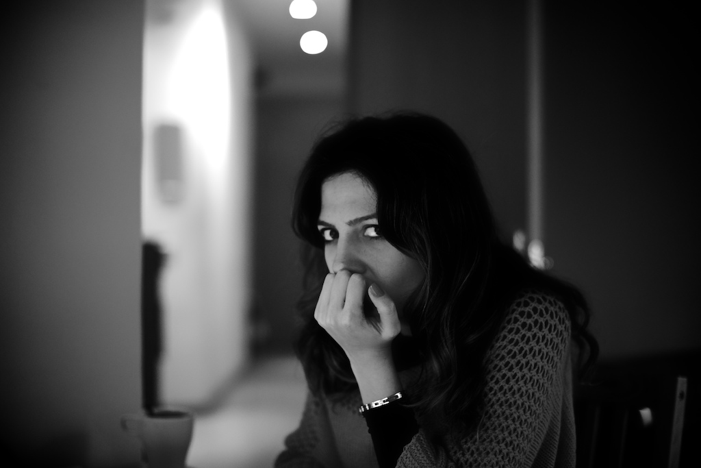 Black and white portrait photograph of a woman with dark hair, hand to face, looking downward in contemplative pose indoors